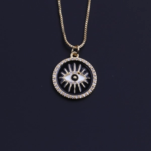 Detail of gold-plated evil eye pendant necklace with sparkling crystal inlay on black background