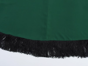 Dettaglio dell'orlo in tessuto verde con fitte nappe di frange nere e trama del materiale