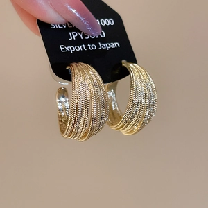 Detail of gold plated C-shaped multi-layered metal hoop earrings held by a hand