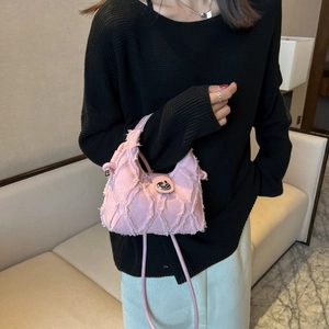 Pink quilted denim crossbody bag with frayed edges and silver twist lock on black knitwear
