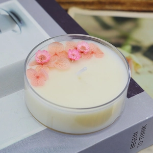 Handmade scented candle with pink dried flowers in a clear jar on a decorative book