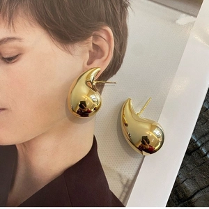 Macro detail of large gold teardrop earrings showing the polished mirror finish and drop shape