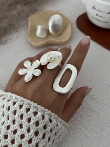 Detail of minimalist silver floral and pearl rings set with brushed metal texture