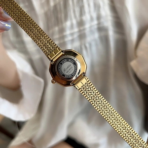 Elegant gold mesh strap watch with stainless steel back, diagonal view on white fabric