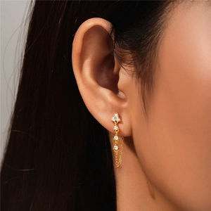Detail of elegant gold drop earrings with white zircon stones and delicate O-chain on ear