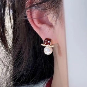 Detail of a dice and pearl earring with red and gold accents on a female model
