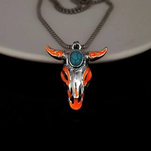 Detail of silver bull skull pendant with orange enamel and turquoise stone on black background