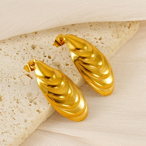 Close-up of golden shell-shaped earrings on a stone base with white silk backdrop