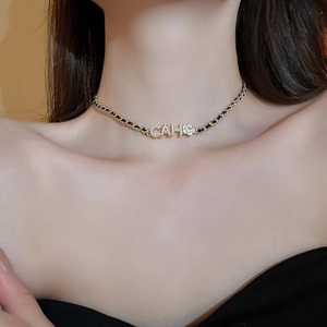 Close-up of gold flower and CAH letter pendant with rhinestones on black woven chain