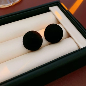 Macro shot of black velvet round stud earrings resting on a white jewelry cushion