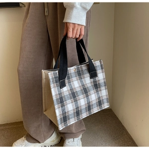 Close-up of canvas tote bag featuring brown grid pattern and black woven handles