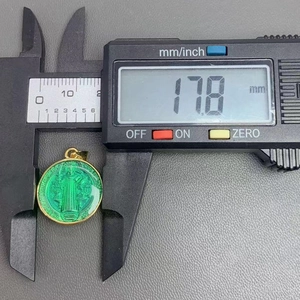 Macro view of 17.8mm green enamel St. Benedict medal pendant shown with digital calipers