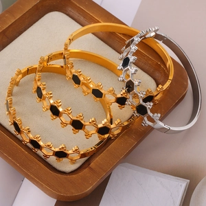Stack of gold and silver honeycomb bangles with black acrylic inlay on a wooden tray