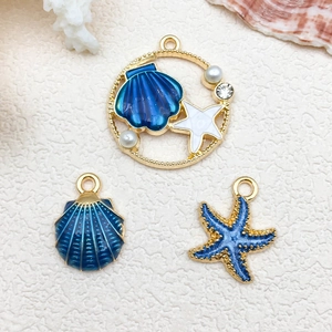 Macro detail of ocean themed gold charms with blue enamel starfish and shell pendants