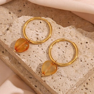 Close-up of golden hoop earrings with translucent orange heart pendants on stone