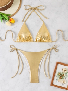 Close-up of golden metallic liquid-effect bikini set on white marble surface
