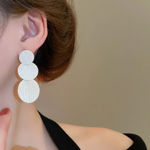 Close-up of geometric brushed silver round drop earrings on model for detailed texture