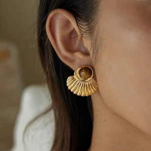 Close-up of a gold fan-shaped earring with a brown tiger eye stone worn on ear