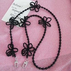 Detail of black beaded chain with flower charms and silver lobster clasp on pink fabric