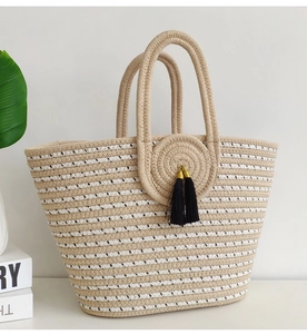 Detail of striped woven straw tote bag featuring a black tassel charm on white background