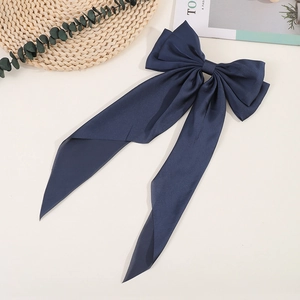 Detail of a large navy blue satin bow hair clip with elegant long ribbons on a flat lay