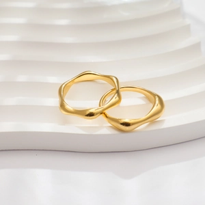Detail of two wavy 18k gold-plated irregular rings on a white textured background