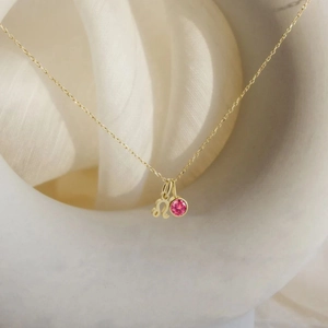 Detail of 18K gold necklace with Leo zodiac charm and round pink gemstone pendant