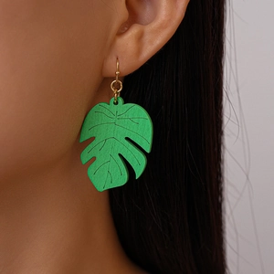 Close-up of vibrant green leaf drop earrings with wood grain texture on model