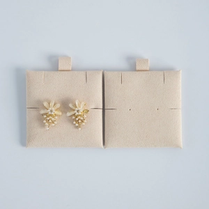 Close-up of cream floral earrings with pearls on a beige velvet jewelry display card