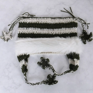 Detailed knit texture of olive and cream striped hat with white faux fur and star tassels