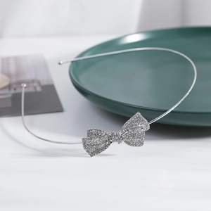 Elegant silver metal headband with a sparkling rhinestone bow on a minimalist white surface