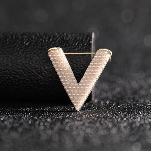 Macro detail of V-shaped gold brooch with inlaid white pearls on dark background