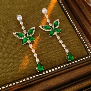 Detail of elegant gold drop earrings with green and white gemstones on velvet