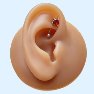 Close-up of minimalist red heart zircon stud on a silicone ear model showing detail