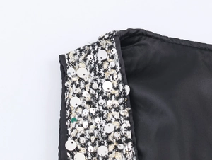 Close-up of black smooth fabric with tweed trim and silver sequins on the dress shoulder