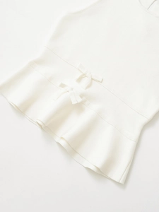 Vue détaillée d'un haut en tricot blanc avec des nœuds élégants et un ourlet ondulé