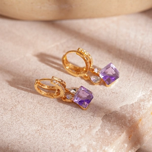 Dettaglio orecchini a cerchio dorati con zirconi viola e cristalli di forma quadrata