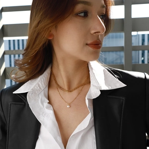 Detail of layered gold necklaces with pearl pendant on a model in a black blazer