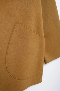 Detailed close-up of pocket stitching and sleeve cuffs on camel wool coat fabric