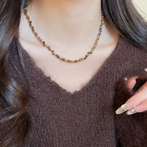 Dettaglio della collana occhio di tigre placcata oro 18 carati indossata su maglia marrone