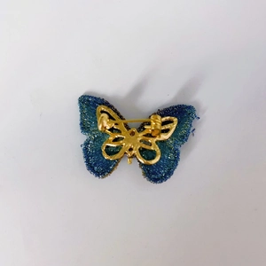 Detailed back view of a blue butterfly brooch featuring a golden metal pin and frame