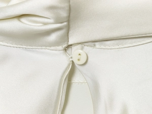 Macro view of white satin dress featuring smooth fabric texture and round button detail