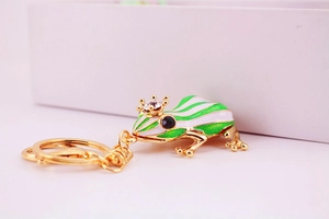 Detailed view of frog keychain with green enamel stripes and crystal crown on gold hardware