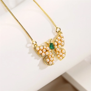 Macro detail of golden butterfly necklace with green gemstone and pearl inlay accents