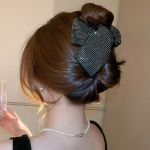 Close-up of a black fabric bow hair claw clip with sparkling rhinestones on an updo hairstyle