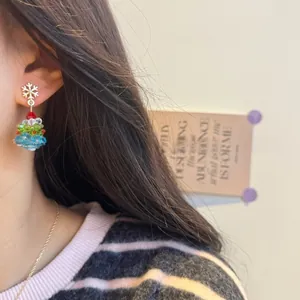 Close-up of beaded Christmas tree earrings with a gold snowflake stud on model