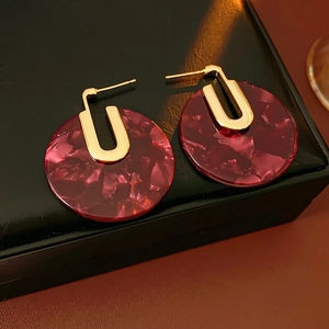 Macro shot of gold-plated circular acetate earrings with purple marble texture on black leather