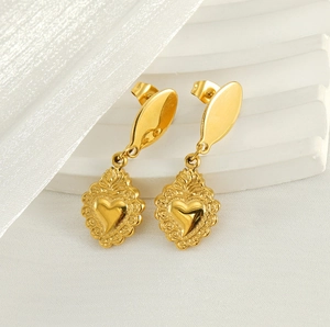 Macro shot of gold-plated sacred heart drop earrings on a white textured backdrop