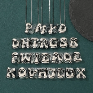 Flat lay of 26 bubbly 3D silver alphabet pendants on textured dark green background