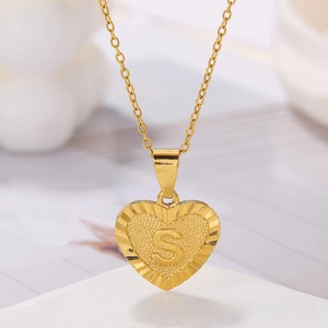Macro shot of gold heart pendant with embossed letter S and sunburst texture detail